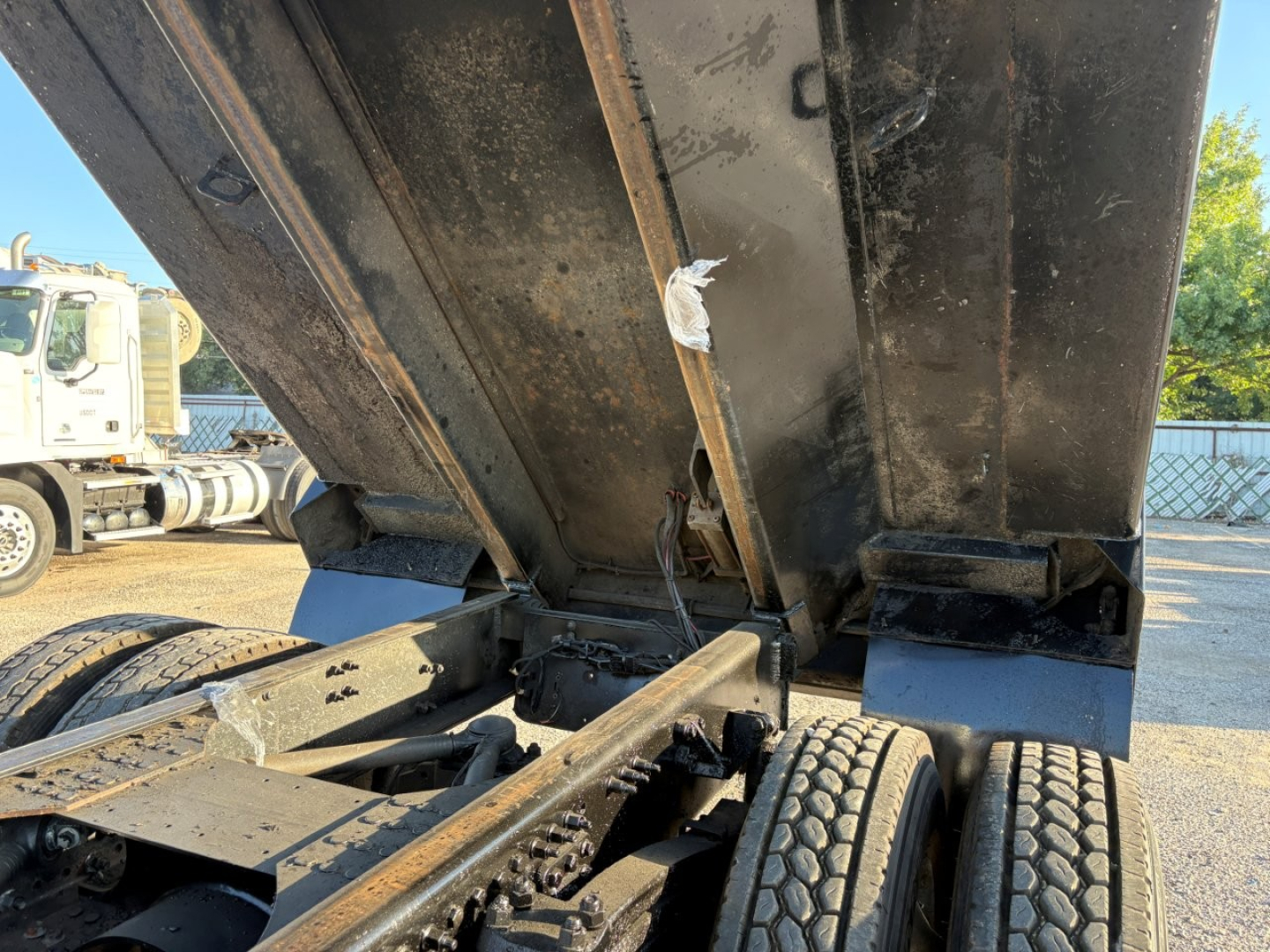 Dump truck bed in raised position showing hydraulic linkage and rear wheels with chassis, Mack GR84F model VIN label not visible.