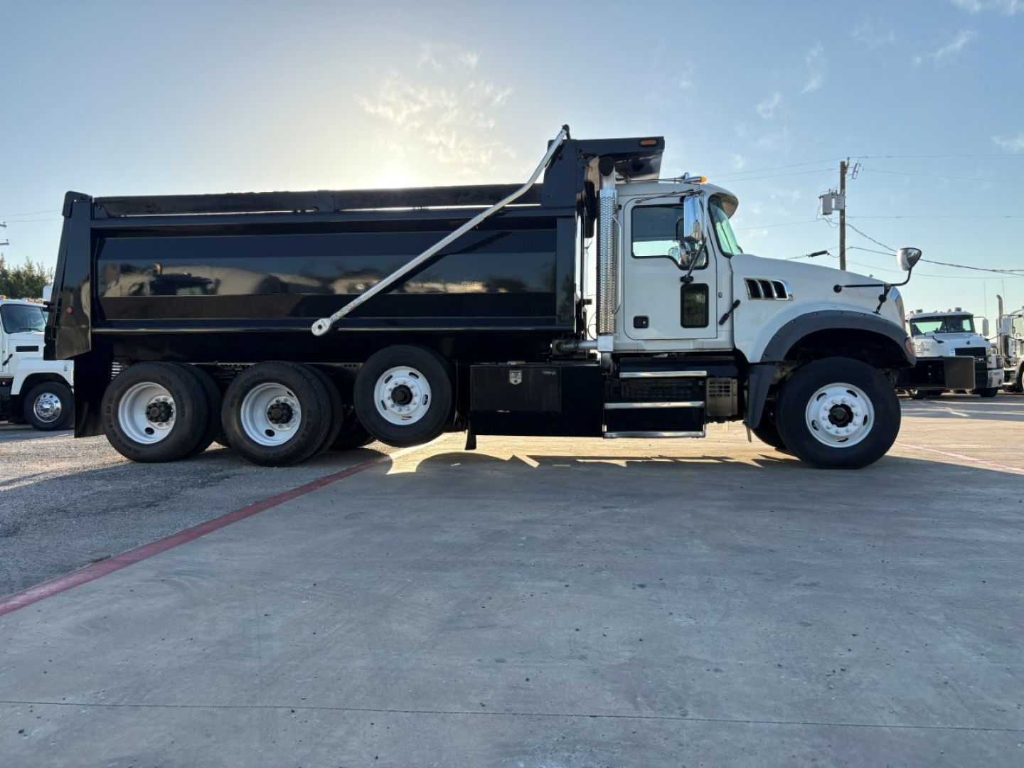Dump truck side view showing Mack GR84F with black dump body and white cab, six wheels, large side-dump hoist, no text visible