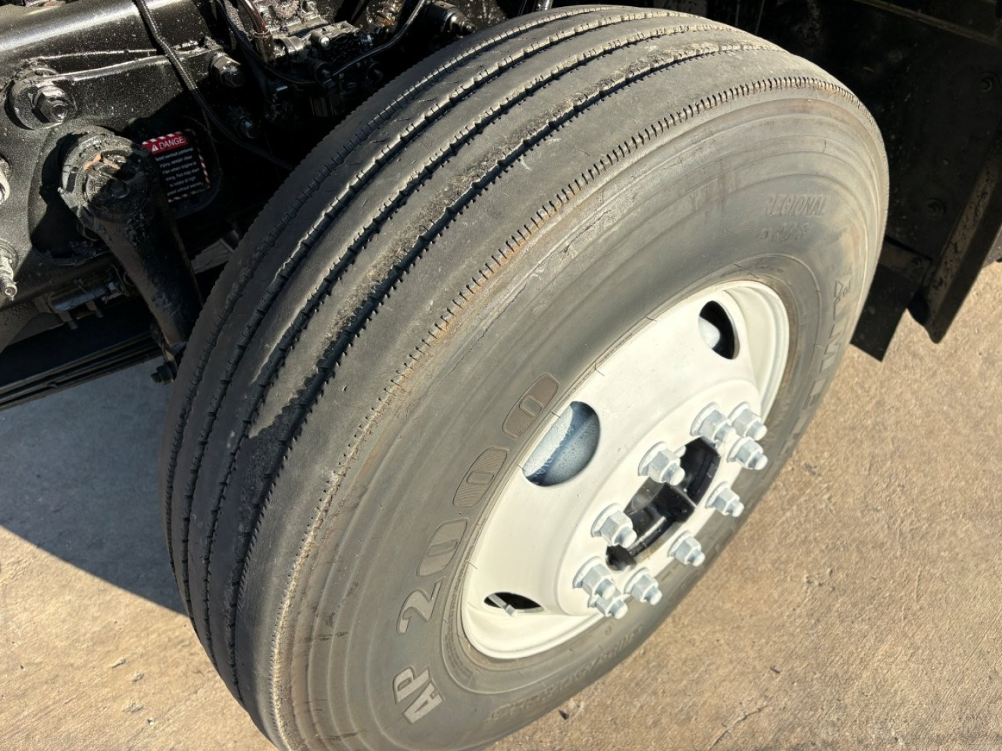 Mack GR84F front wheel and tire assembly showing 2-axle dual rear? wheel with lug nuts and hub, portion of chassis and suspension visible.