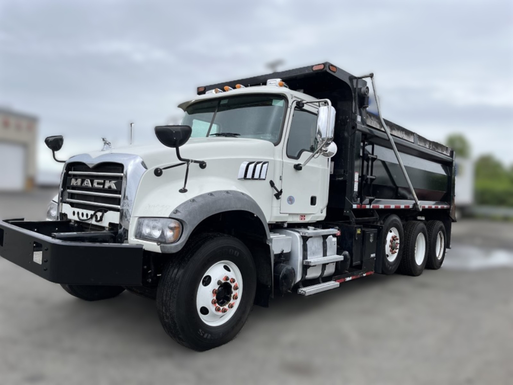Mack GR84F dump truck in-service showing front grille with MACK badge, white cab, black dump bed, dual rear axles, warning lights on cab roof.