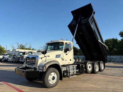 Truck showing a white Mack GR84F dump truck with raised black dump bed.