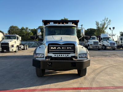 Truck front view of a 2023 Mack GR84F dump truck with large grille, bumper, and dual mirrors; other trucks in background