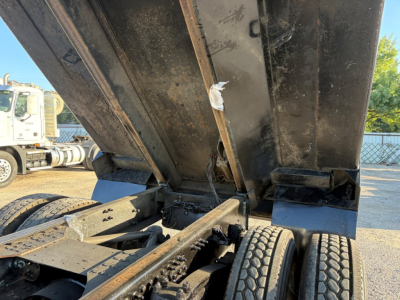 Dump truck bed in raised position showing hydraulic linkage and rear wheels with chassis, Mack GR84F model VIN label not visible.