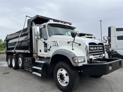 Dump truck showing Mack GR84F dump bed with white cab and black bumper, front grille with MACK branding, six wheels visible, side mirror, and hydraulic bed components.