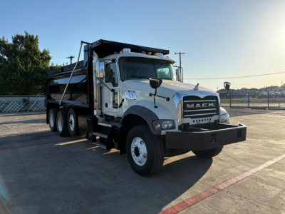 Dump truck showing a white Mack GR84F dump truck with black grille, three-axle rear, and large front bumper.