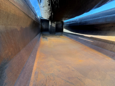 Dump truck bed interior showing rust-toned metal floor and sidewalls with a centered chock area and shadowed top edge.