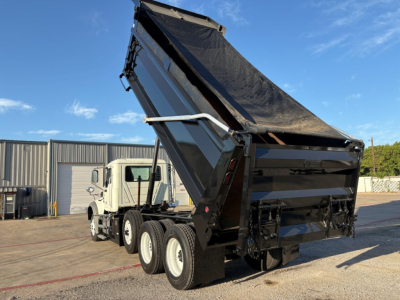 Mack GR84F dump truck with raised bed in loading position, dual rear axles, black dump bed and white cab, side view showing hydraulics and wheels.