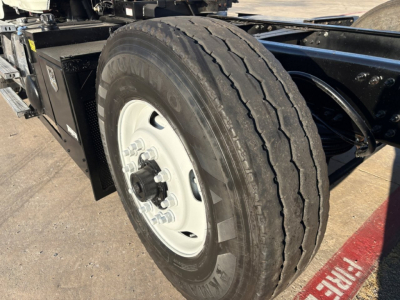 Mack GR84F truck chassis showing tandem wheel and tire with white rim, text on tire sidewall visible, and nearby black battery box.