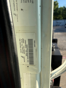 Truck door jamb label with VIN sticker and barcode visible on a Mack truck component, showing model/brand information and serial numbers.