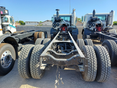 Mack TE64E chassis rear view showing dual rear axles and exposed driveline with power unit engines on trucks in background.