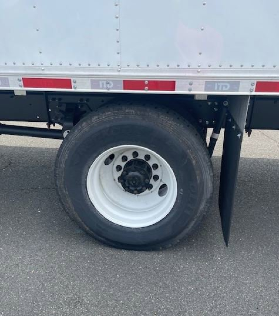 Hino L6 box truck wheel area showing white steel wheel with black center hub and tire, undercarriage, side reflective tape along cargo body.
