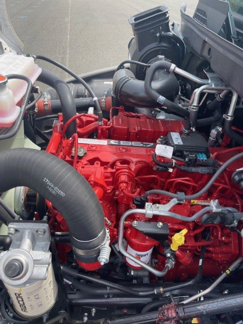 Box van truck engine bay showing red engine with hoses, black turbo housing, coolant reservoir, and various metal lines.