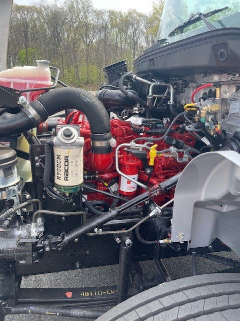 Engine bay of 2026 Hino L6 box van showing Bosch-Rexroth? no, actually RACOR filter labeled 'RACOR' on fuel filter, red engine components, hoses, and coolant reservoir visible..