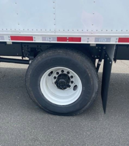 Hino L6 box truck wheel area showing white steel wheel with black center hub and tire, undercarriage, side reflective tape along cargo body.