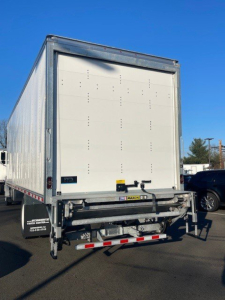 Rear view of a 2026 Hino L6 box van truck showing closed cargo doors and rear underrun protection, metallic frame, and bumper with reflective tape.