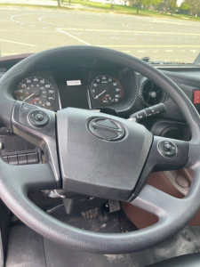 Steering wheel and dashboard of a Hino L6 truck cab showing instrument cluster and control stalks.