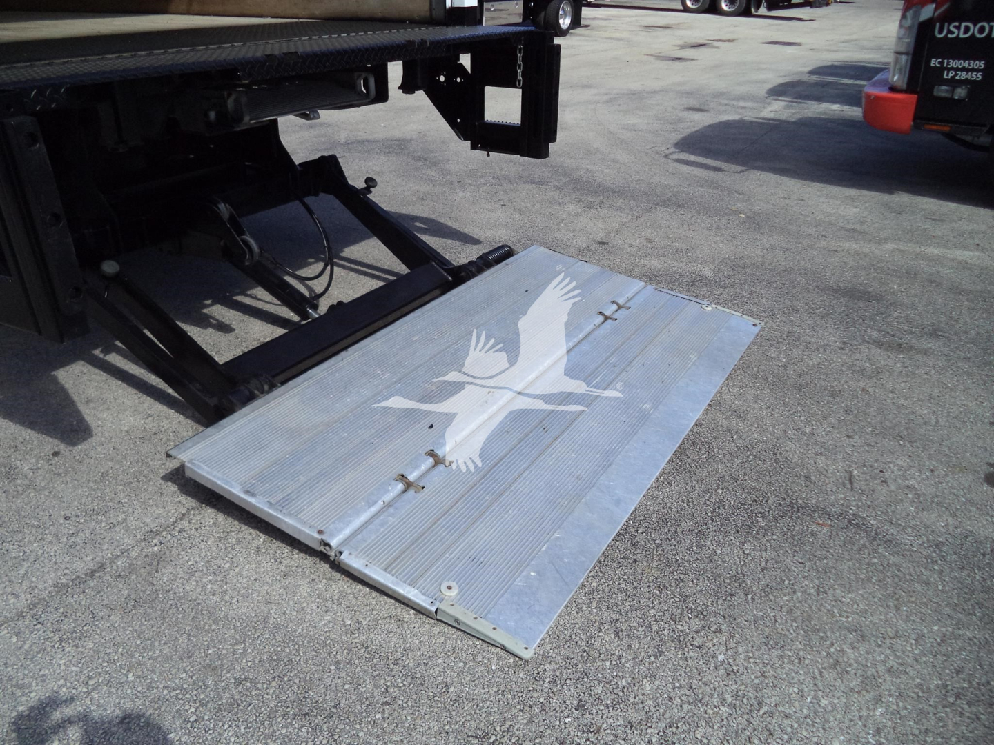 Isuzu NPR HD truck with lowered aluminum ramp featuring a graphic eagle logo, rear of truck visible.