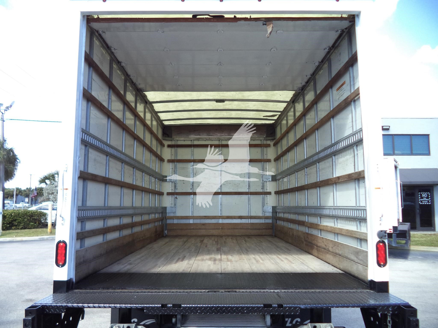 Isuzu NPR HD box truck cargo area seen from rear with empty wooden floor and side rails.