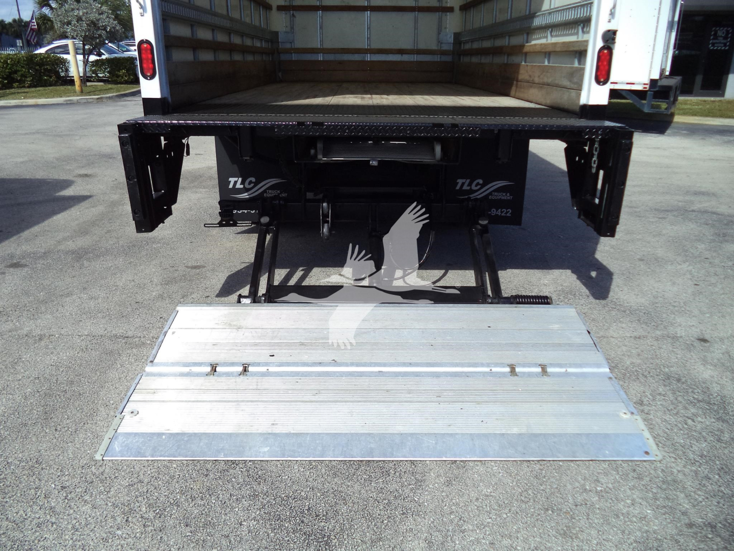 Isuzu NPR HD box truck rear view with extended aluminum ramp lowered to ground, showing tailgate mechanism and rear undercarriage.