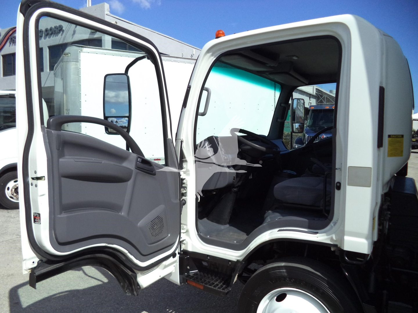 Isuzu NPR HD truck cab interior with driver door open, showing steering wheel, dashboard, and seating; exterior white cab in view.