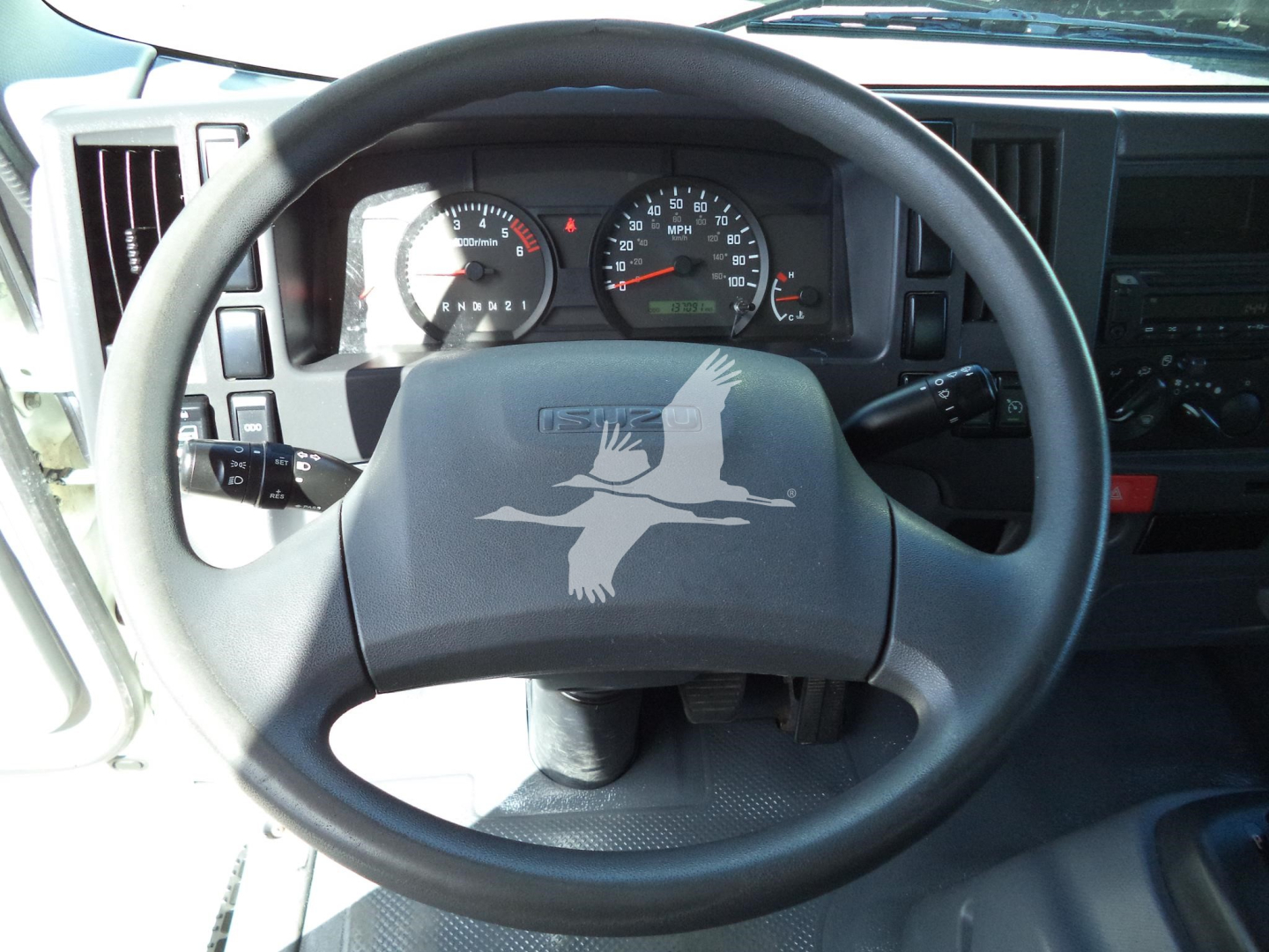 Isuzu NPR HD cockpit with steering wheel and instrument cluster; dashboard controls and gauges behind wheel.
