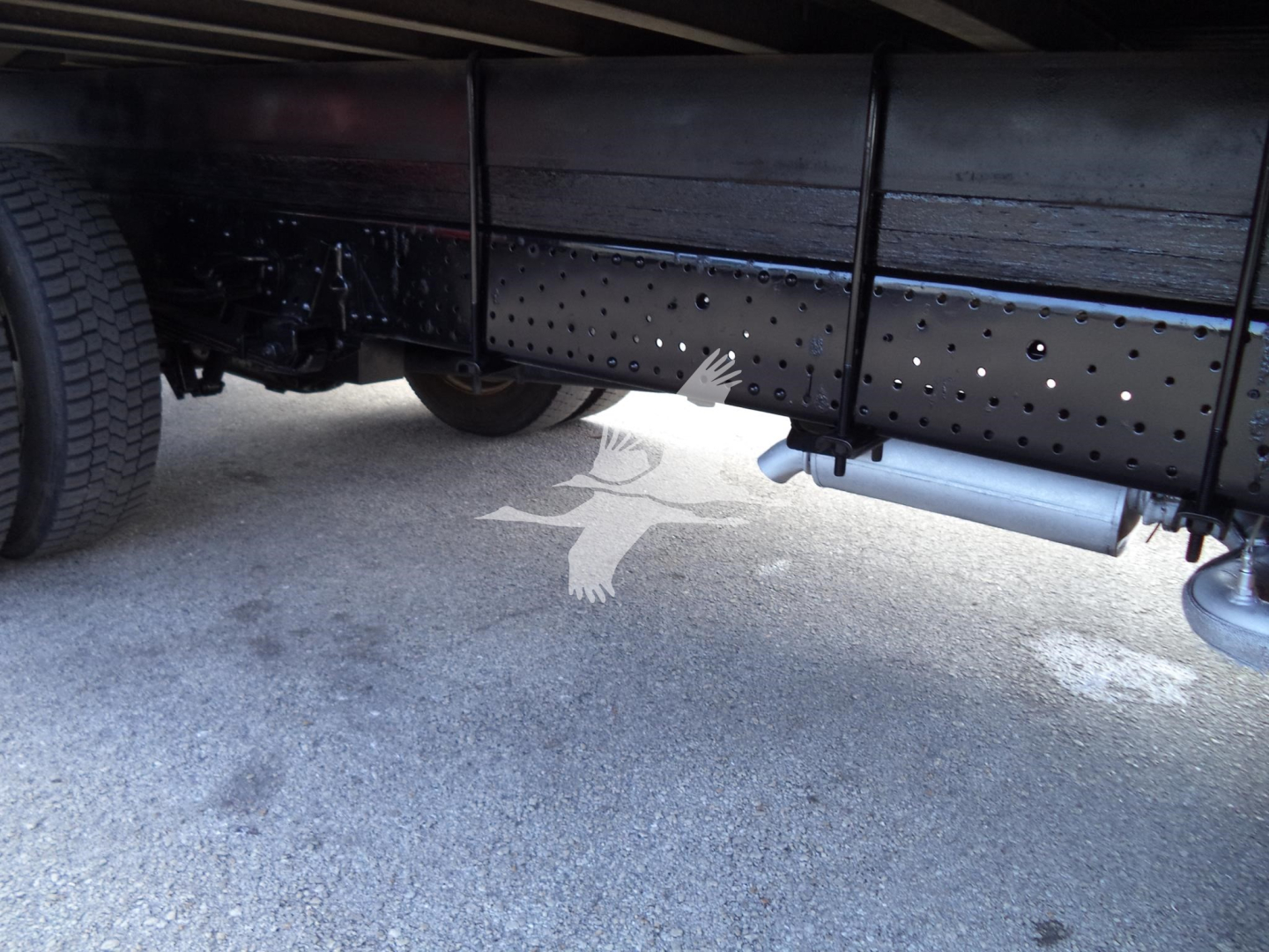 Isuzu NPR-HD truck undercarriage showing frame and side exhaust/step rail with perforated frame holes and underbody components.