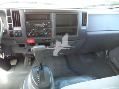 Dashboard of a 2020 Isuzu NPR HD truck showing gear shifter, radio, climate controls, and empty stereo slot, with a watermark overlay on the center console area.