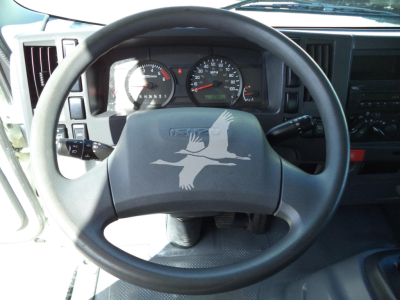 Isuzu NPR HD cockpit with steering wheel and instrument cluster; dashboard controls and gauges behind wheel.