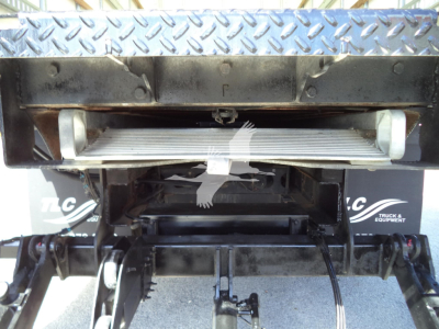 Isuzu NPR HD truck bed area showing hydraulic mechanism and load bed support with diamond-plate pattern and silver ladder rails.