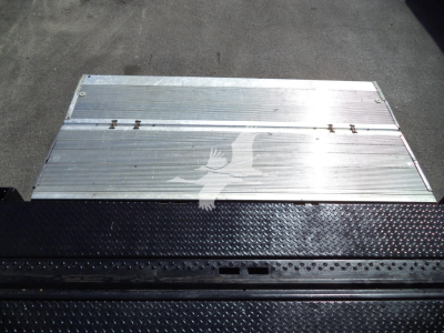 Isuzu NPR HD truck bed ramp/platform with aluminum surface, visible screws, and diamond plate step edges.