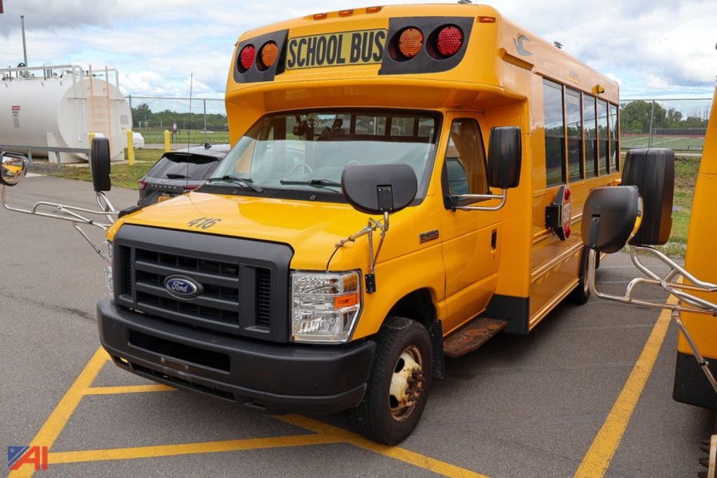 Ford-blue-bird E-Series school bus front-left view showing exterior with yellow paint and 'SCHOOL BUS' signs on top front window and stop arms.