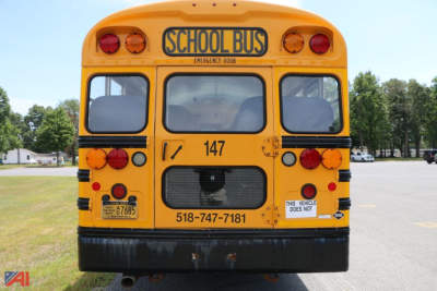 School bus rear view showing 147 and 518-747-7181, emergency door label, 'SCHOOL BUS' sign, yellow body with red and orange lights, license plate area.