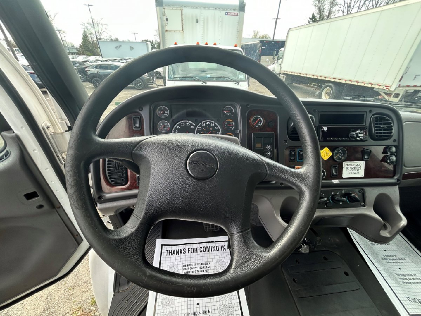 Dashboard and steering wheel of a Freightliner M2 106 interior showing gauges, steering wheel, center console with controls, and ignition area.
