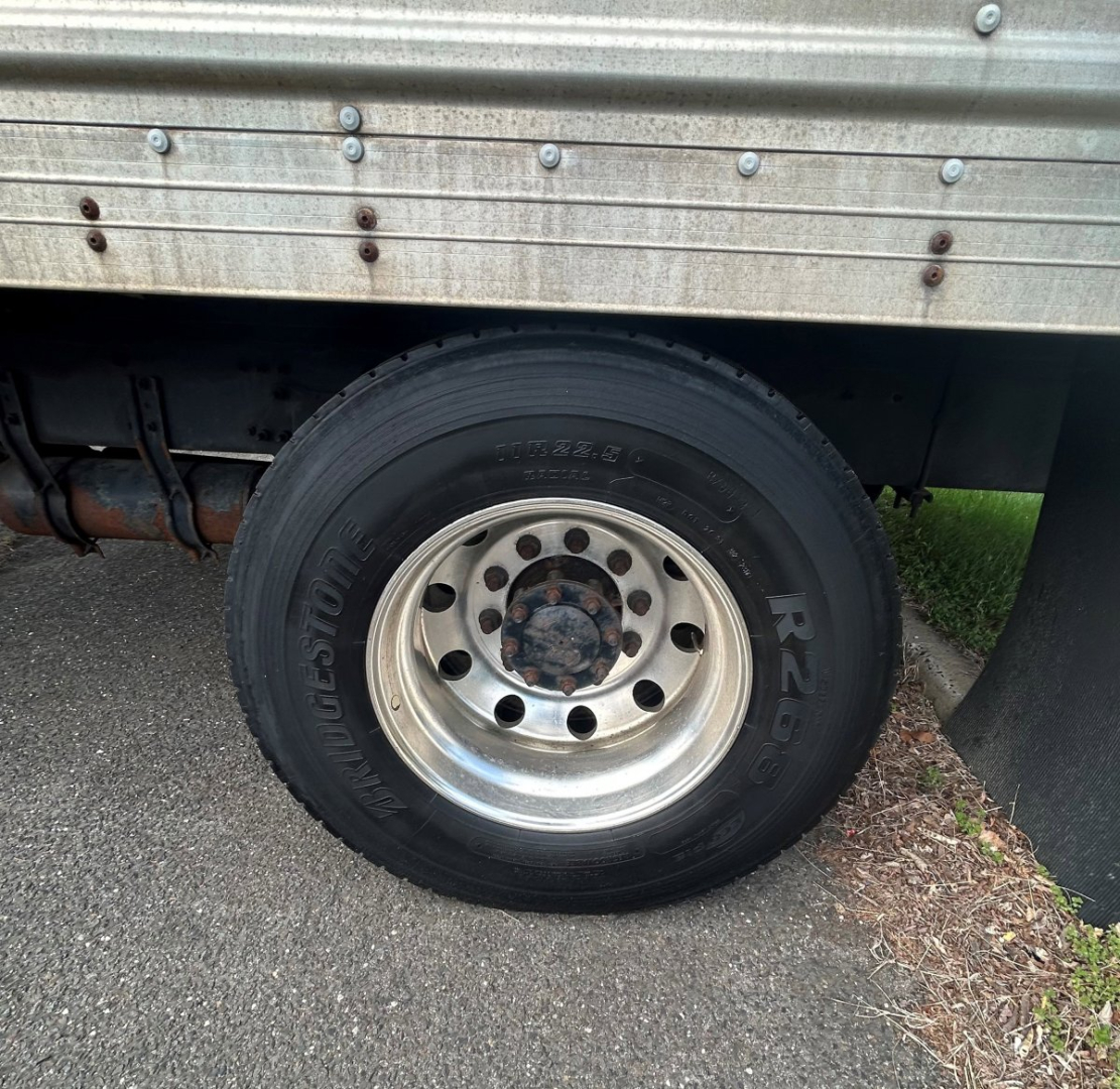 Wheel and fender area of a Freightliner M2 106 MEDIUM D truck showing a front wheel with black tire and silver steel rim