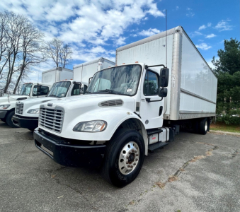 Freightliner M2 106 medium duty box truck, white cab with large box body, front-left view, several similar trucks in background.