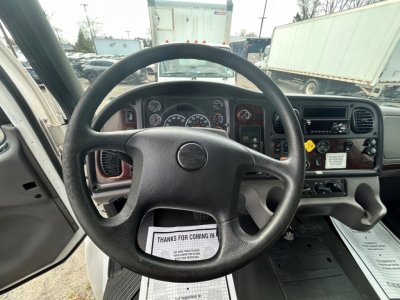 Dashboard and steering wheel of a Freightliner M2 106 interior showing gauges, steering wheel, center console with controls, and ignition area.