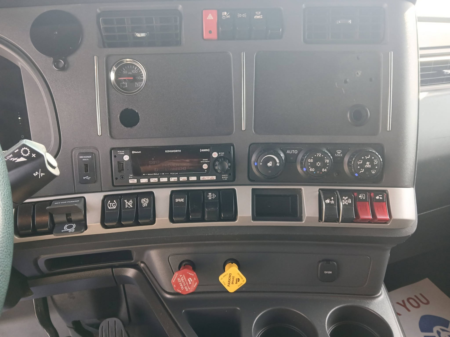 Dashboard of a Kenworth T680 truck showing various controls, gauges, and two colored knobs (red and yellow) with surrounding switches.