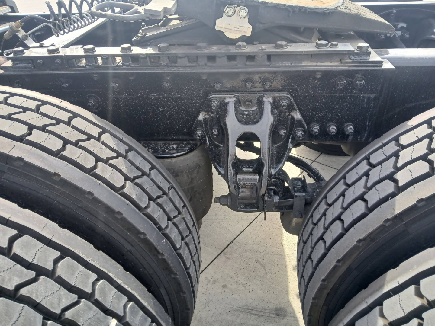 Trucks chassis rear view showing dual rear axles and fifth wheel mount on Kenworth T680, with visible suspension components and bolts.