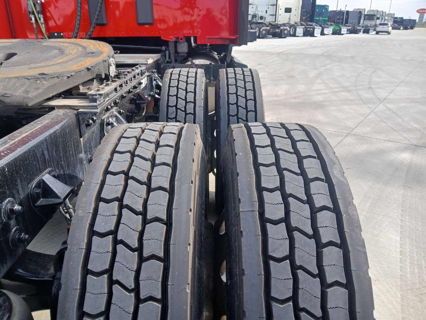 Two rear truck axles and tires of a 2023 Kenworth T680 tractor showing dual rear tires and part of the red cab in the background.