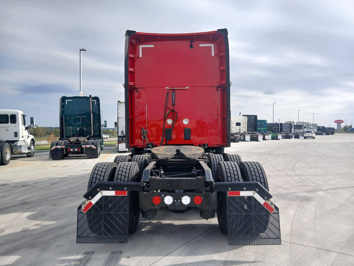 Kenworth T680 tractor rear view showing red cab, dual rear axles, and mudflaps in a truck yard.