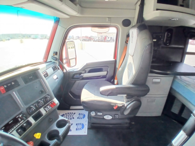 Kenworth T680 truck interior cab showing driver seat and dashboard with steering wheel, center console, and sleeping area in back. Visible door panel and window.