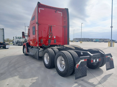 Kenworth T680 tractor chassis rear view showing dual rear axles, red sleeper cab, black fifth wheel area, mudflaps, and rear lights. No visible serials or labeling readable.