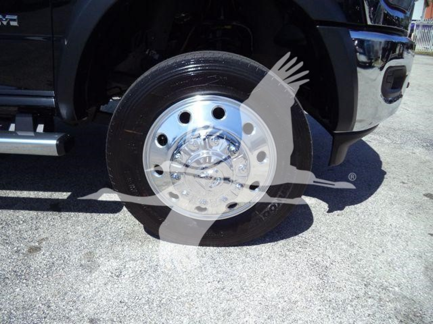Truck front wheel with chrome hub and black tire, partial front bumper; watermark overlays the image.