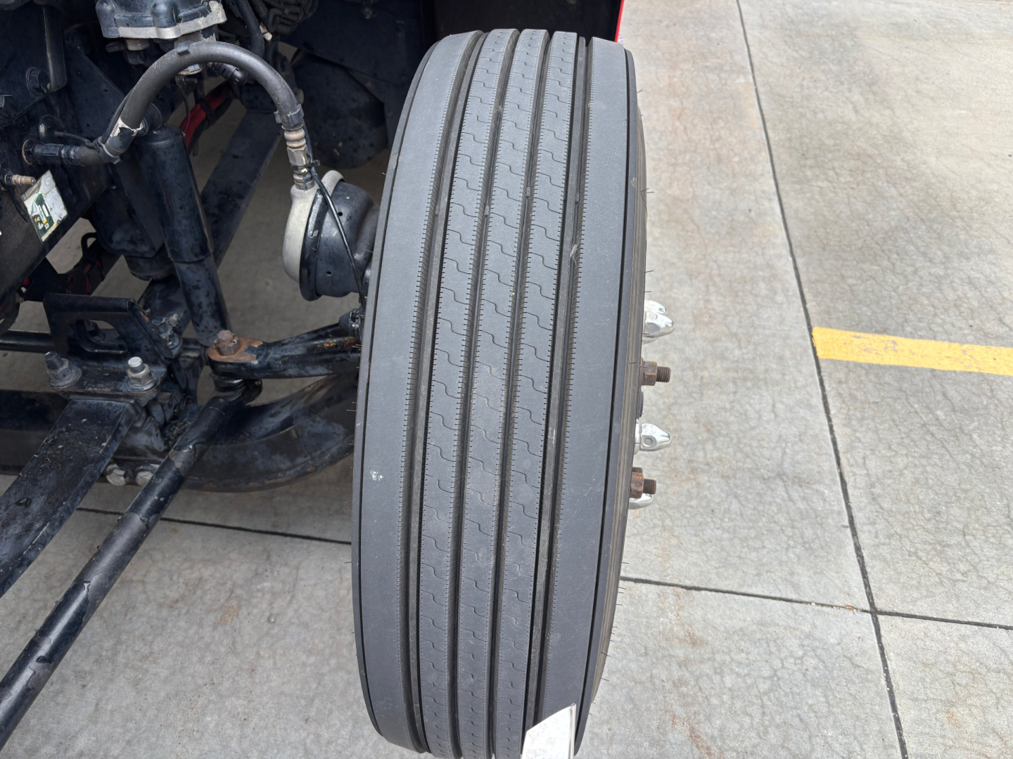Peterbilt 579 front axle area showing dual tires and wheel hub with lug nuts, chassis components, and tire treads visible.