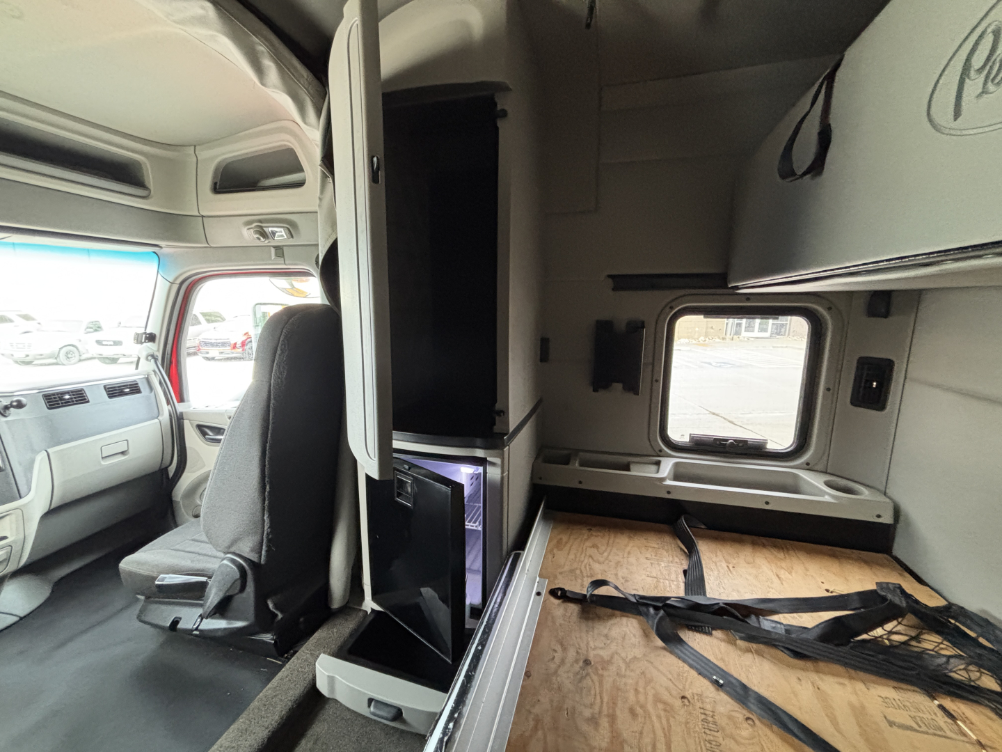 Truck cab interior of a 2020 Peterbilt 579 showing sleeper area with wooden floor, vertical cabinet, and side window.