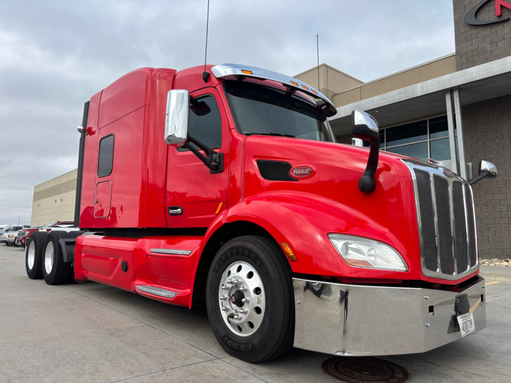 Peterbilt 579 conventional sleeper truck in red, front-right view with chrome bumper and large grille; Dual rear axles visible; badge on hood