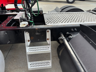 Peterbilt 579 chassis rail with metal steps, ladder, and battery connections visible under cab area in-service condition.