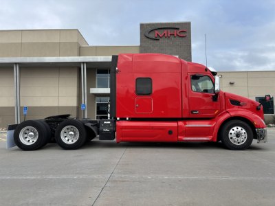 Peterbilt 579 conventional sleeper truck in red side view showing cab, sleeper, dual rear axles, and dealership building in background