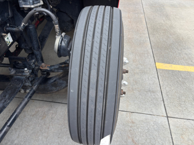 Peterbilt 579 front axle area showing dual tires and wheel hub with lug nuts, chassis components, and tire treads visible.