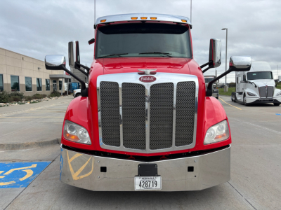 Peterbilt 579 truck front view showing large chrome grille, red hood, and bumper with license plate; mirrors extend from sides; headlights visible.